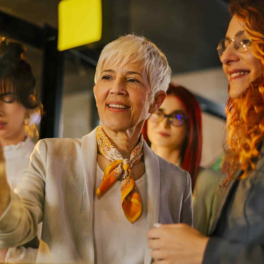 Creativity-innovation-performance-resilience-productivity Manager and staff in funky business attire talking in front of a glass window post it notes on it.